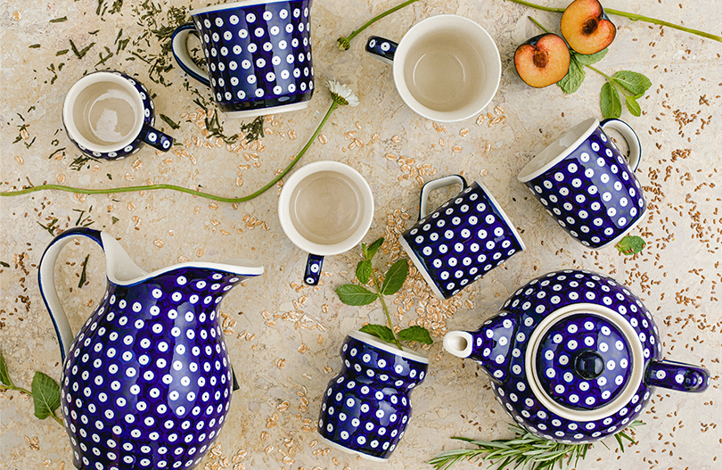 Ein Krug aus Keramik liegt neben einer Teekanne in einem tiefen Blau. Becher und Tasse wurden beigestellt.